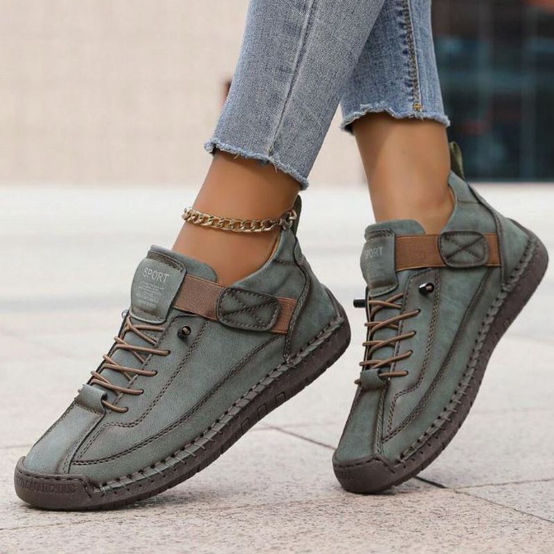 Sage green Nora trainers featuring a lace-up front, secure hook-and-loop strap, contrast stitching, and a durable flat sole.