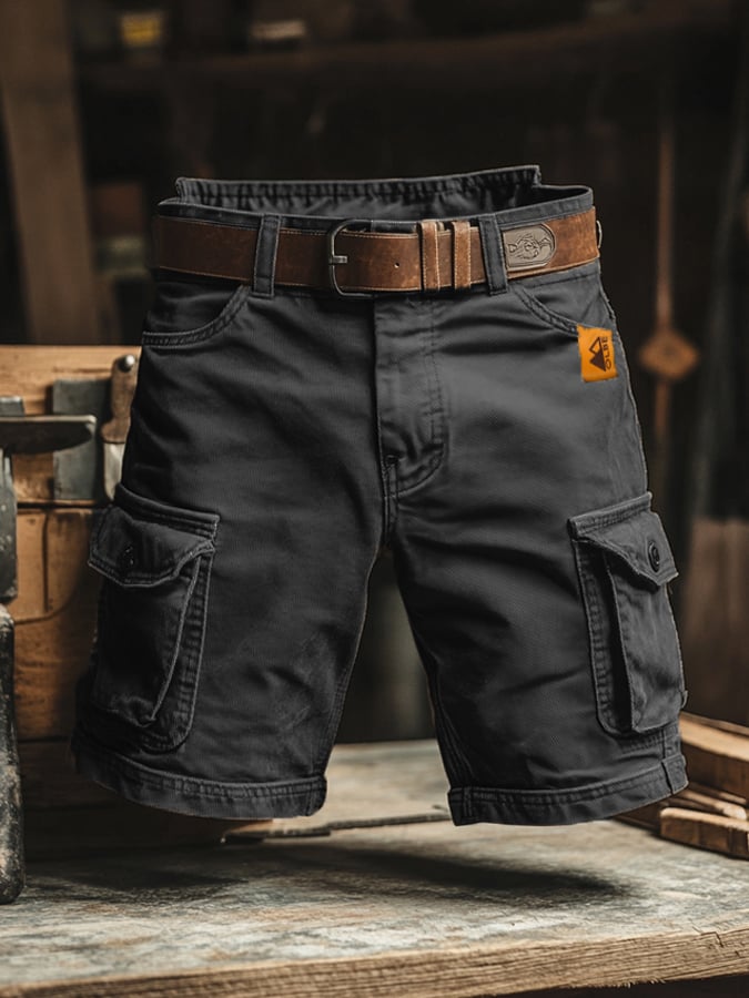 Charcoal grey knee-length cargo shorts with side pockets, a brown leather belt, and an orange brand tag on a workbench.