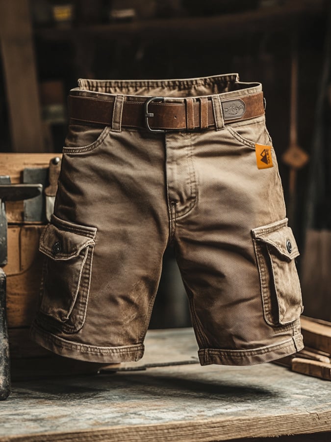Rugged brown knee-length cargo shorts with side pockets, a leather belt, and a small orange logo tag on a wooden workbench.
