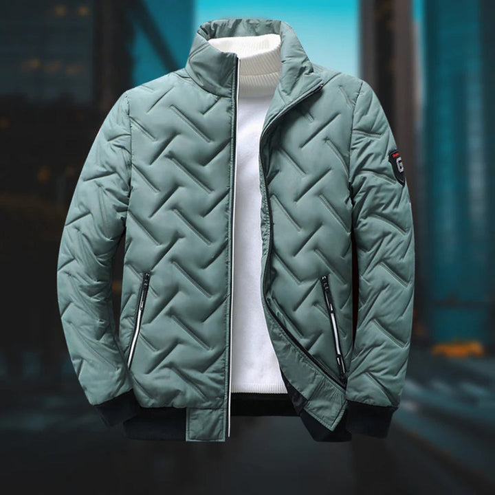 Sage green quilted chevron jacket with a stand-up collar, zip pockets, and black ribbed hem over a white turtleneck.