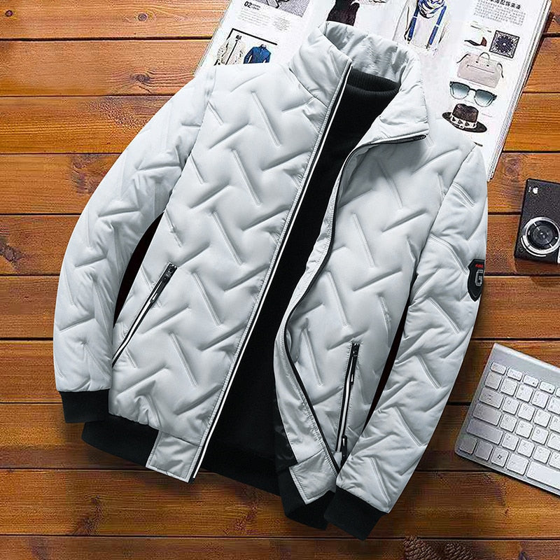 Light grey men's quilted jacket with chevron pattern, stand-up collar, zip pockets, and black ribbed cuffs on wood background.