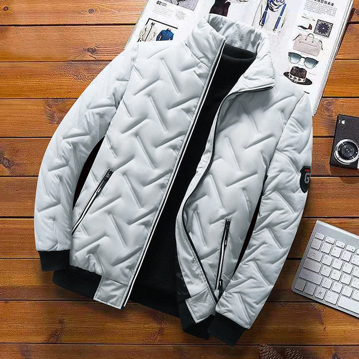 Light grey men's quilted jacket with chevron pattern, stand-up collar, zip pockets, and black ribbed cuffs on wood background.