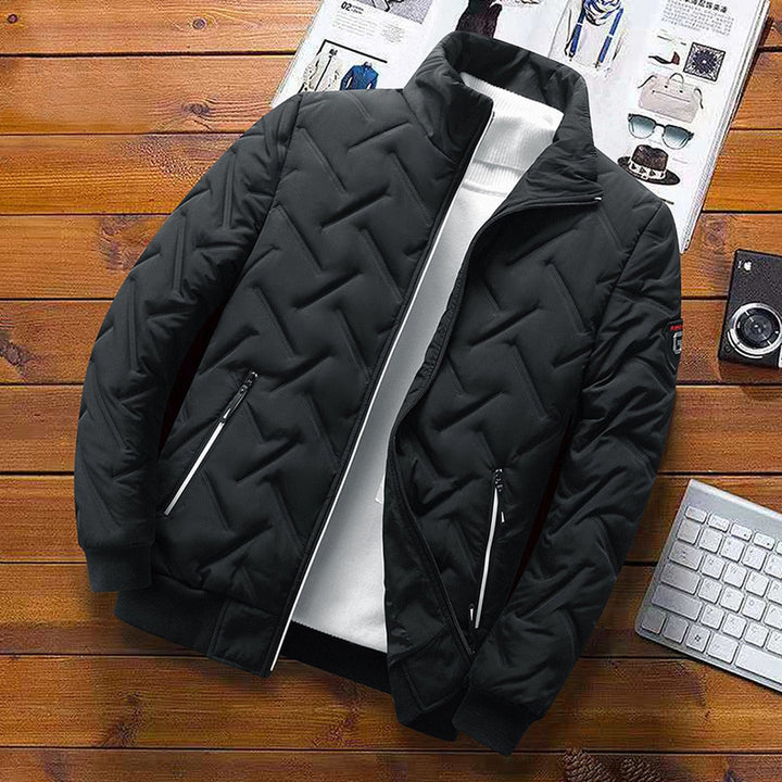 Black quilted chevron padded jacket with a stand-up collar, zip pockets, and ribbed cuffs on a wooden background.
