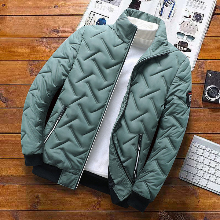 Sage green quilted chevron jacket with a stand-up collar, zip pockets, and black ribbed cuffs on a wooden background.