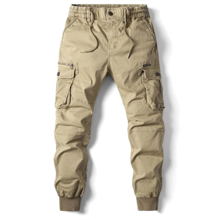 Beige cotton utility cargo trousers with an elasticated drawstring waist, multiple side pockets, and cuffed ankles.