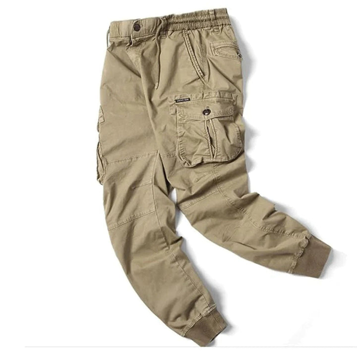 Beige cotton utility cargo trousers with an elasticated drawstring waist, multiple flap pockets, and cuffed ankles.