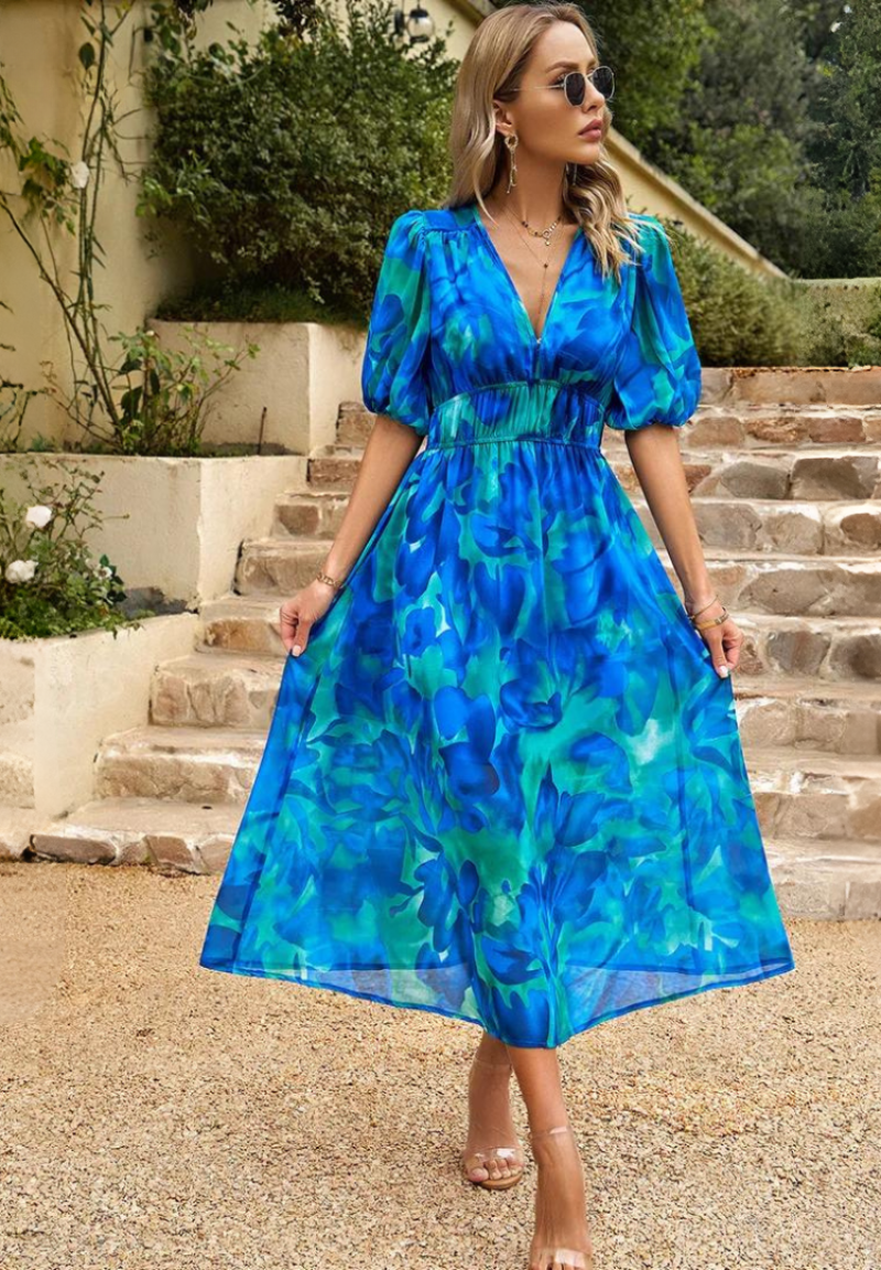 Woman wearing a blue and teal floral midi dress with a V-neckline, gathered waist, and romantic puff sleeves.