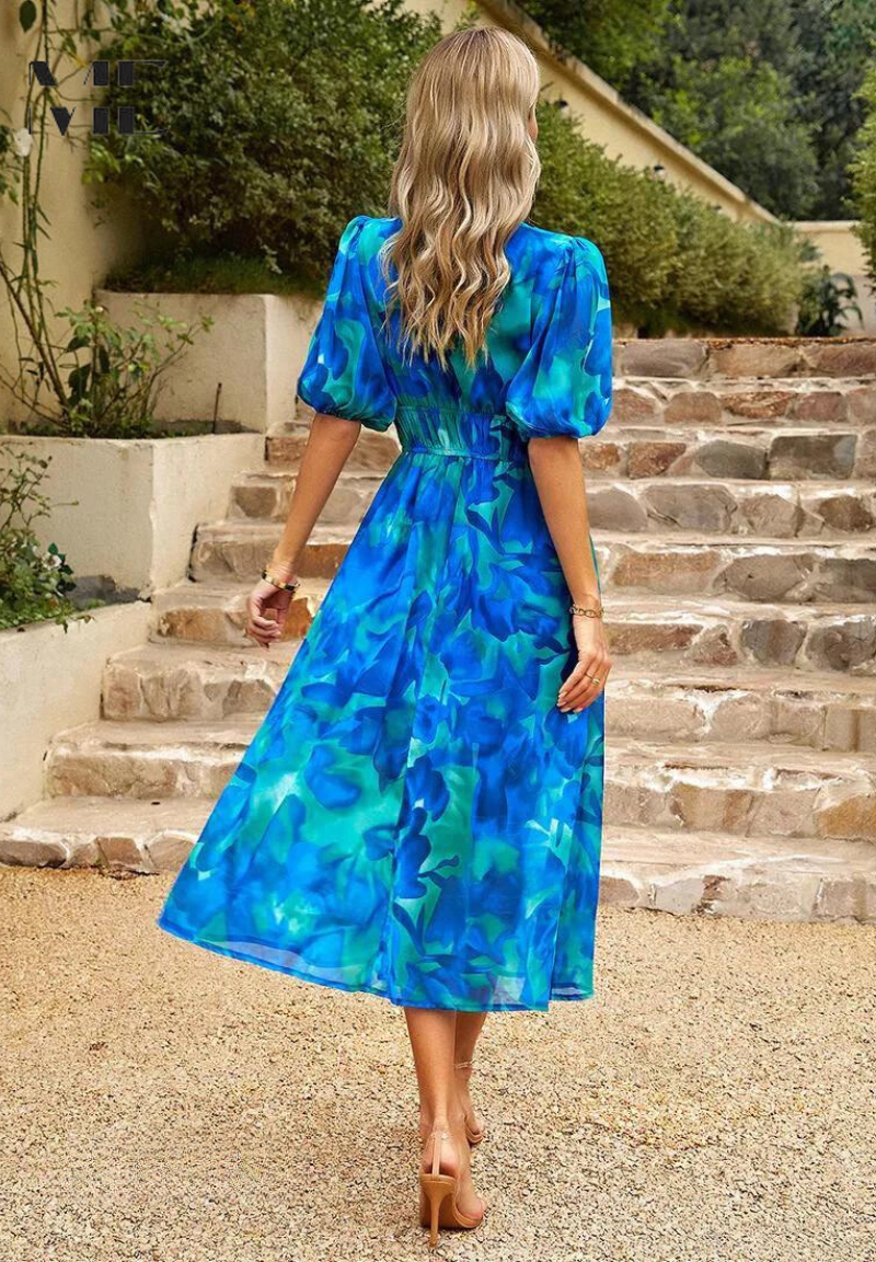 Woman wearing a blue and teal floral midi dress with puff sleeves and a gathered waist, standing on stone stairs.