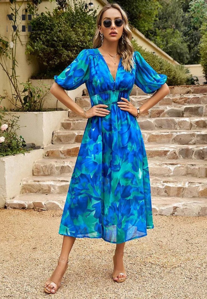 Woman wearing a blue and teal floral midi dress with a V-neckline, gathered waist, and romantic puff sleeves.