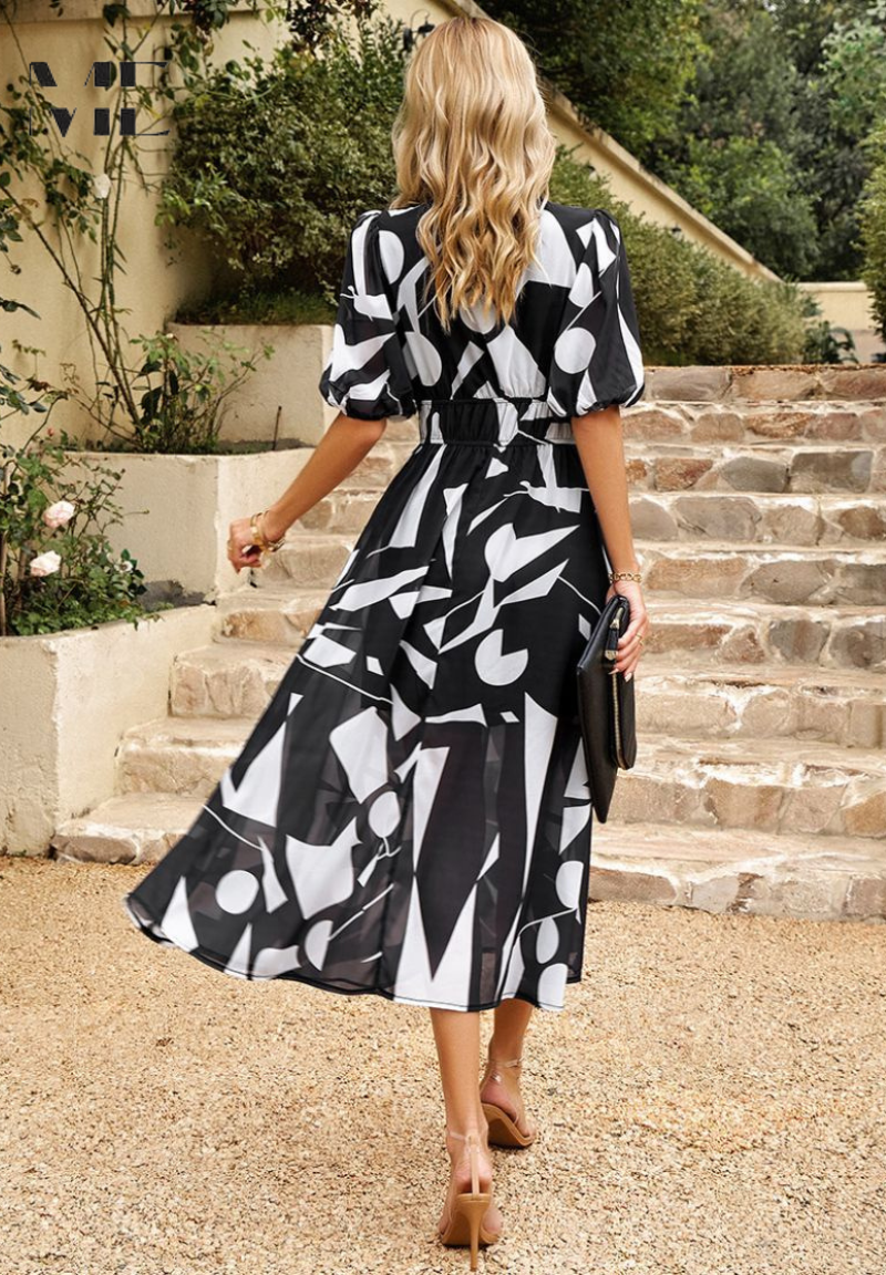 Woman wearing a black and white geometric print midi dress with puff sleeves and a gathered waist, walking outdoors.