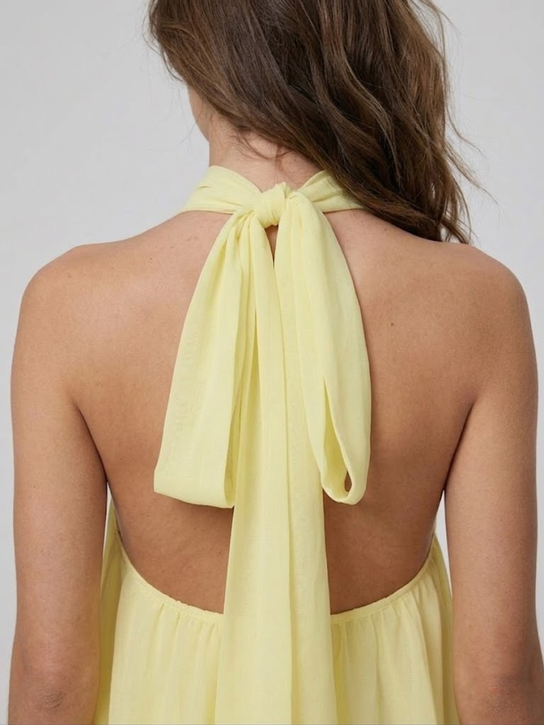Back view of a light yellow halter mini dress featuring a self-tie neck fastening and an elegant open back design.