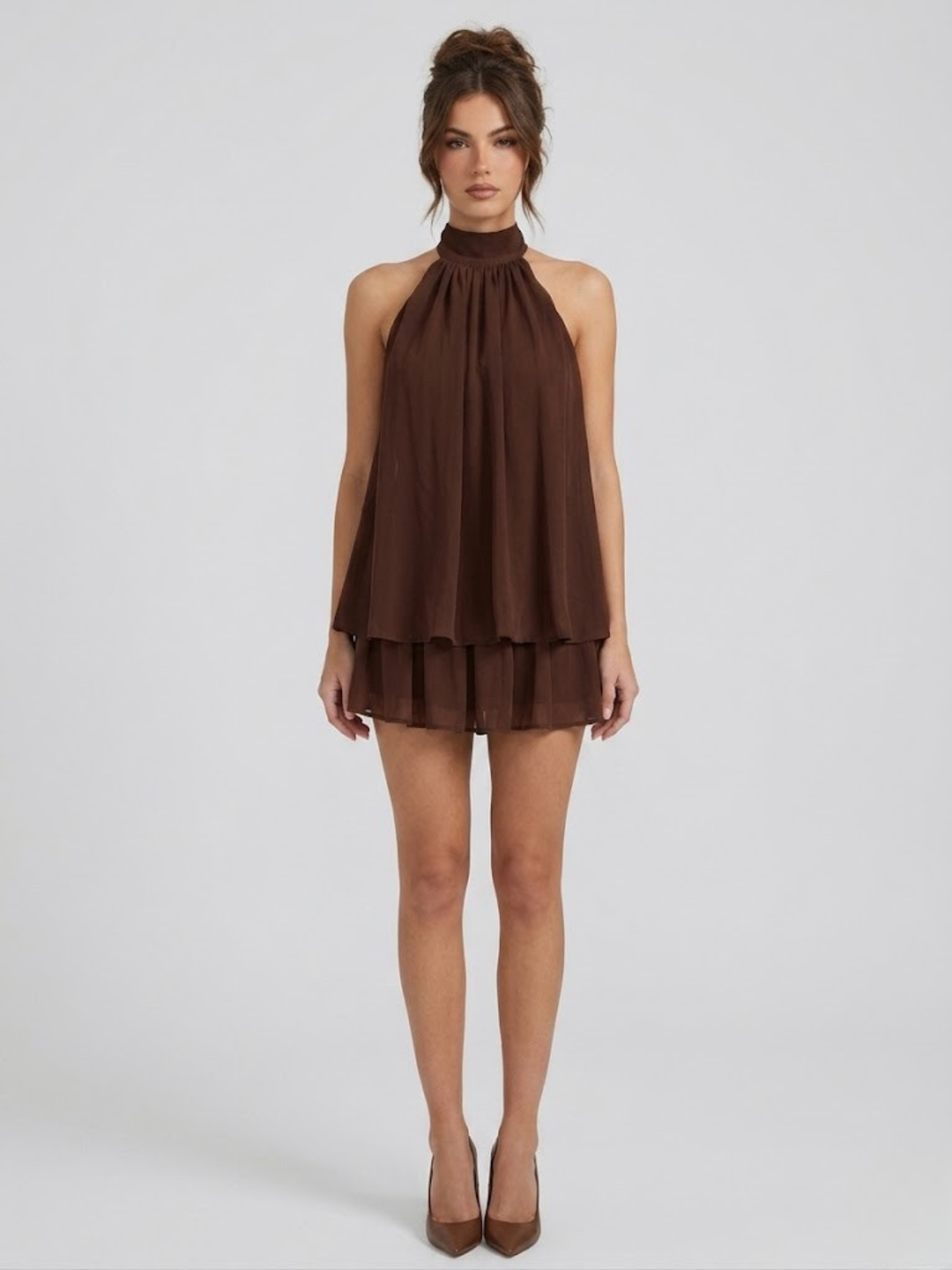 Brown halter neck mini dress with a tiered ruffle hem and lightweight, flowy fabric on a model.