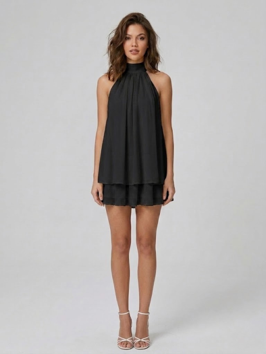 Black halter neck mini dress with a tiered ruffle hem and relaxed swing silhouette worn by a woman.