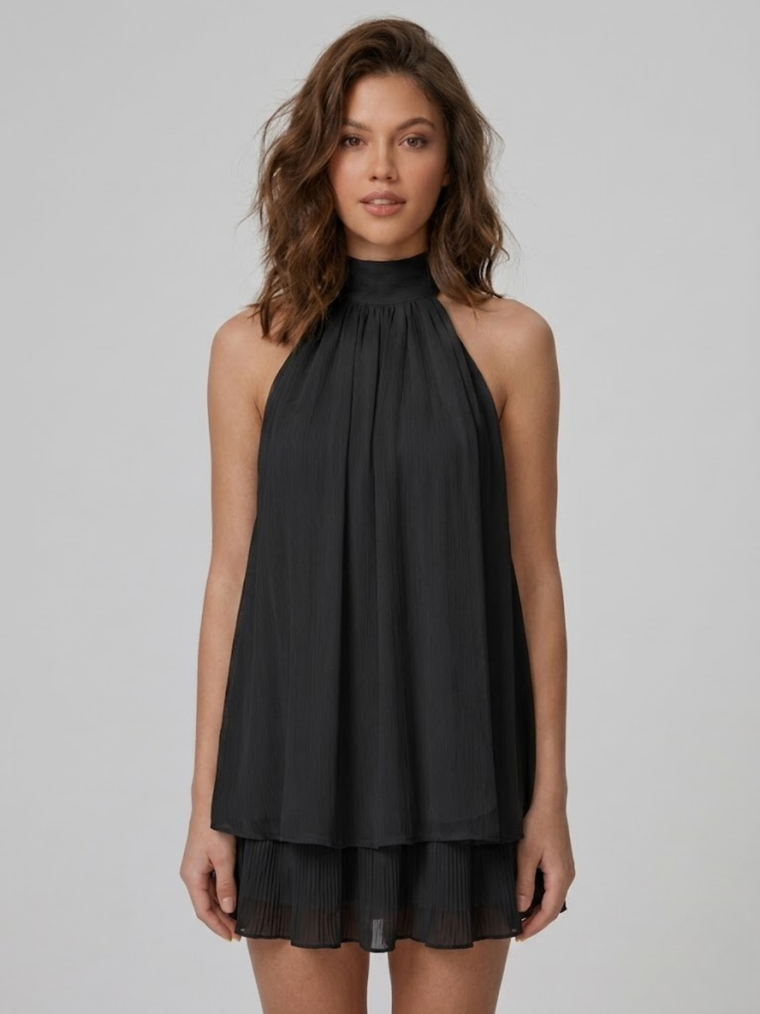 Model wearing a black, pleated halter-neck mini dress with a tiered ruffle hem and lightweight, flowy fabric.