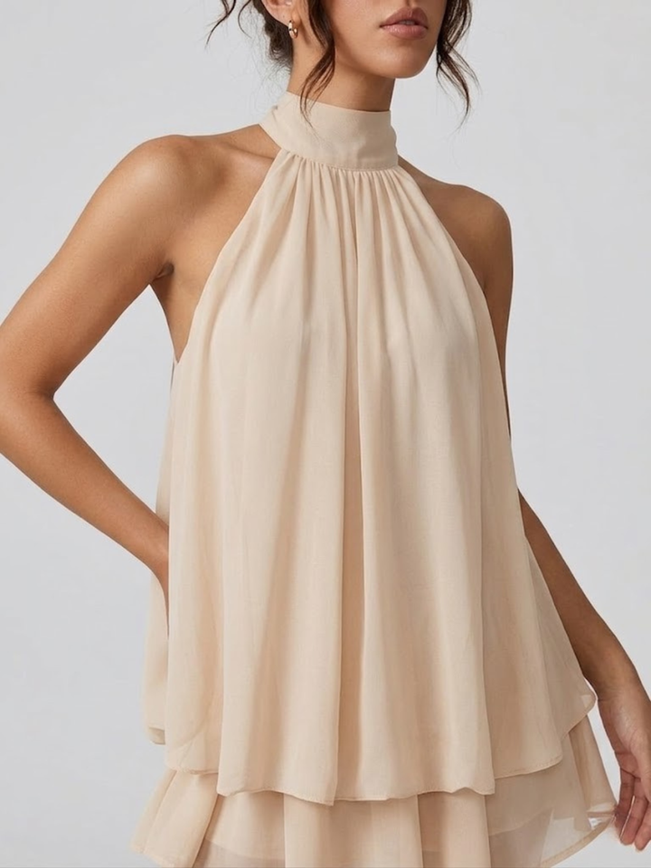 Beige halter neck mini dress with a tiered ruffle hem and flowy, lightweight fabric on a model.