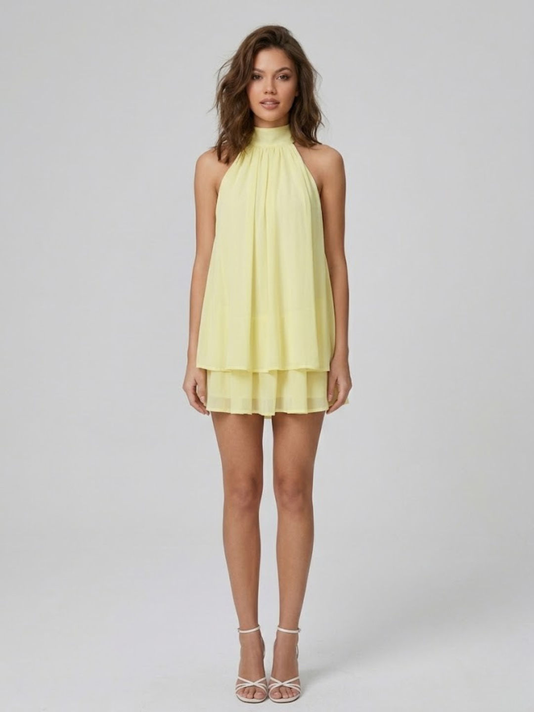 Model wearing a light yellow, sleeveless halter mini dress with a tiered ruffle hem and lightweight, airy fabric.