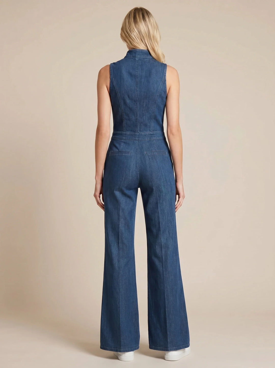 Back view of a sleeveless blue denim jumpsuit with a fitted bodice, stand collar, and flared legs on a model.