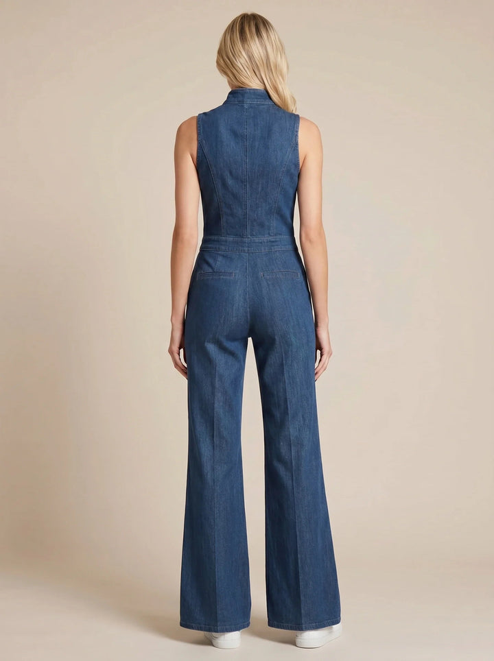 Back view of a sleeveless blue denim jumpsuit with a fitted bodice, stand collar, and flared legs on a model.