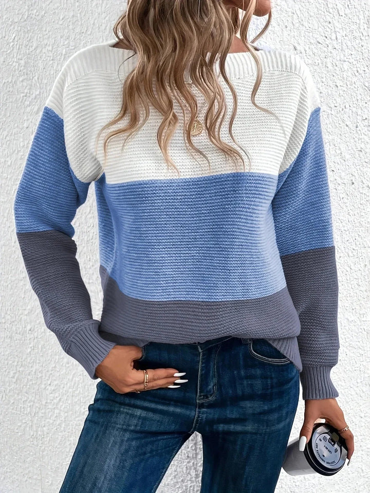 Woman wearing a chunky ribbed colour block jumper in white, light blue, and grey with a relaxed boat neckline.