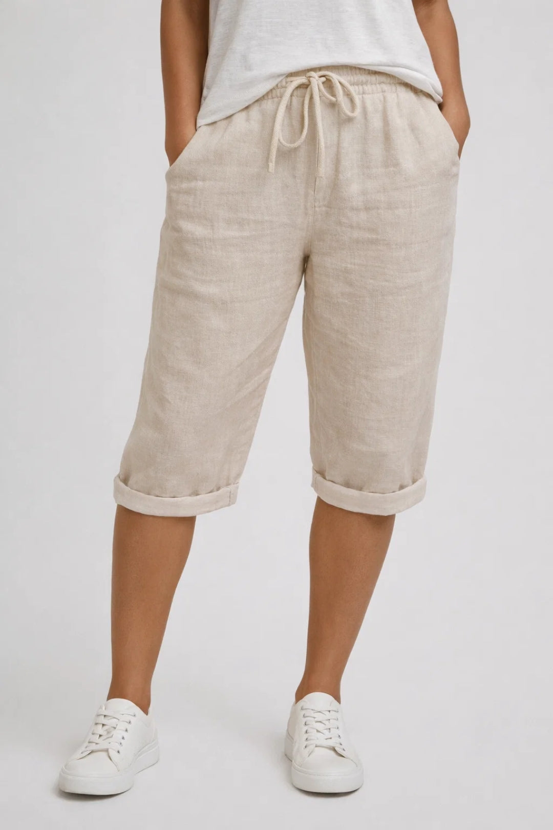 Beige linen knee-length shorts with a drawstring elastic waist, side pockets, and rolled-up hems.