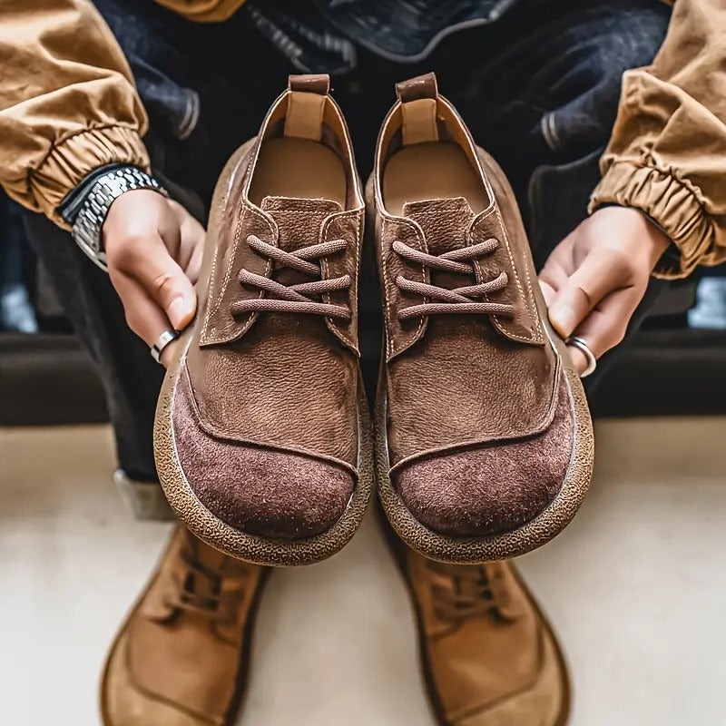 Brown leather lace-up walking shoes with a rounded toe and textured rubber sole held by a man in casual attire.