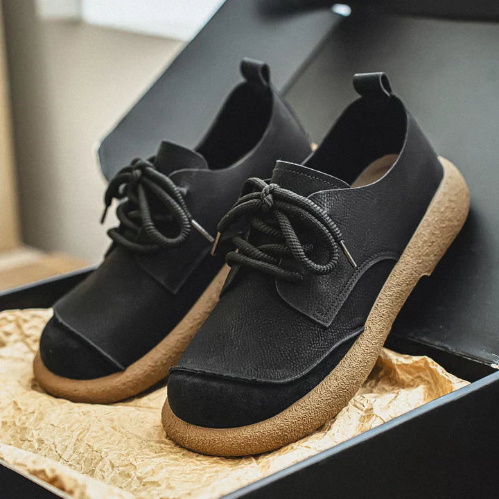 Black leather lace-up walking shoes with a textured tan cushioned sole in a box.