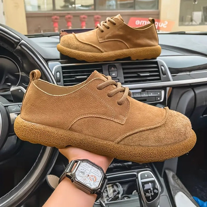Tan suede lace-up walking shoes with a textured rubber sole held in front of a car dashboard.