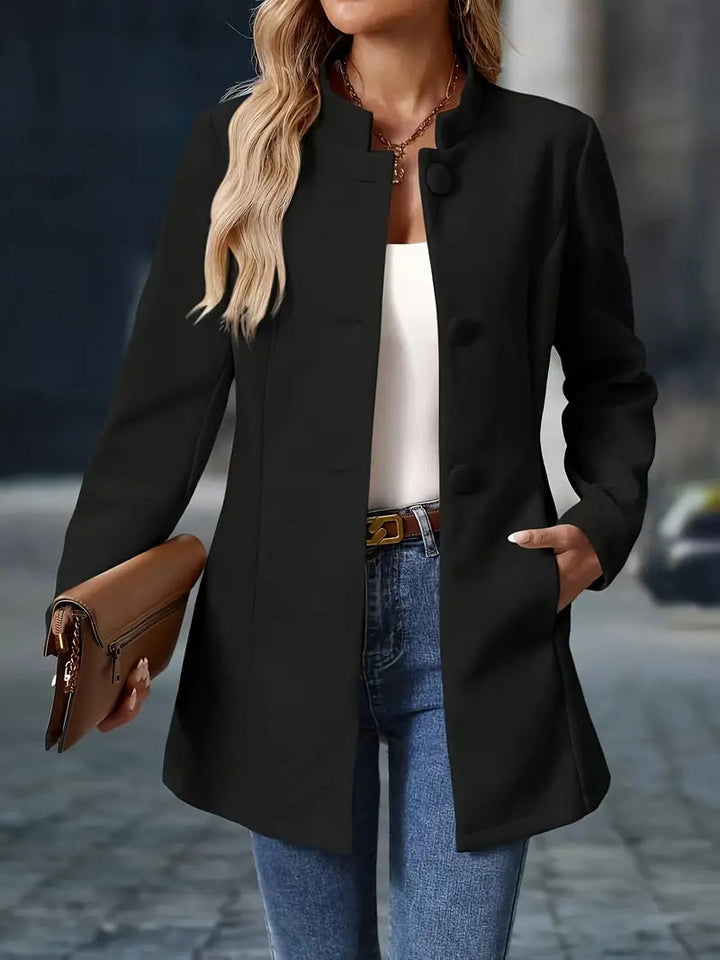 Black mid-length coat with a stand collar, covered button front, and tailored waist worn over jeans.
