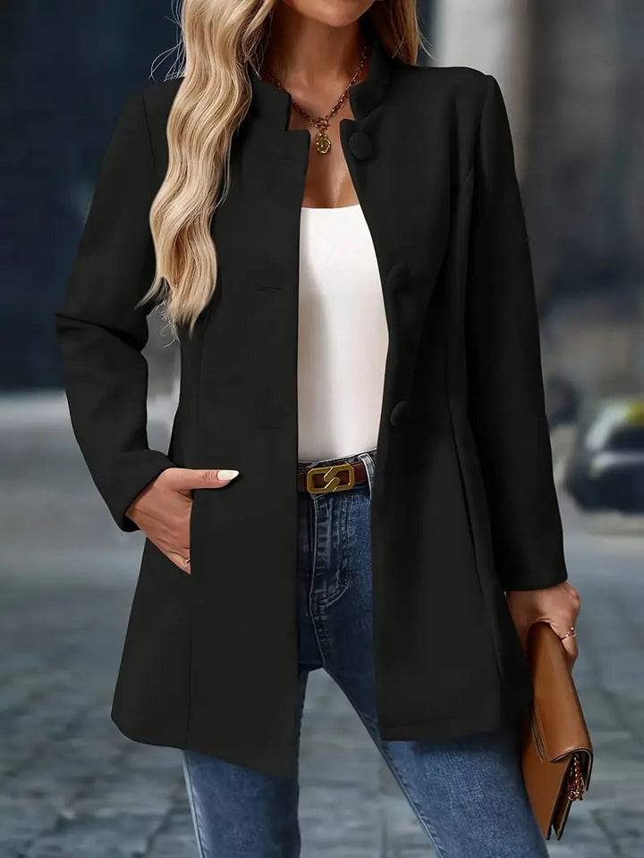 Black mid-length coat with a stand collar, button-front closure, and tailored waist worn over jeans.