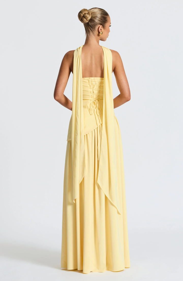 Back view of a yellow strapless corset maxi dress with a lace-up back and elegant draped scarf panels.