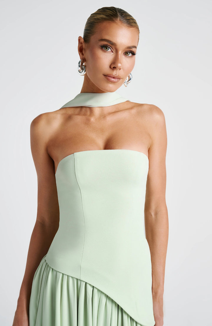 Model wearing a sage green strapless corset maxi dress with draped scarf neck detail and structured bodice.