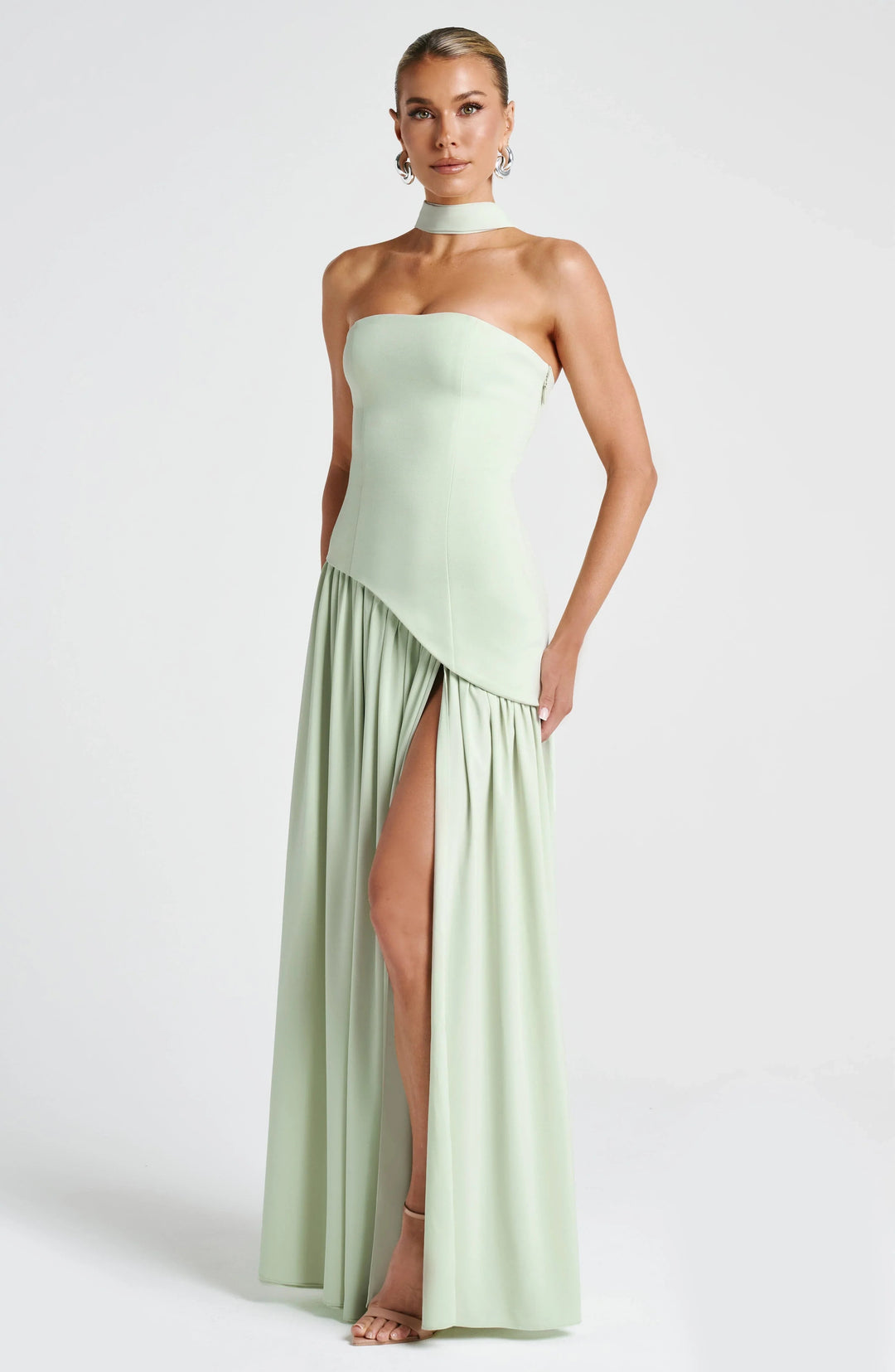 Model wearing a sage green strapless corset maxi dress with a high leg slit and draped scarf detail.
