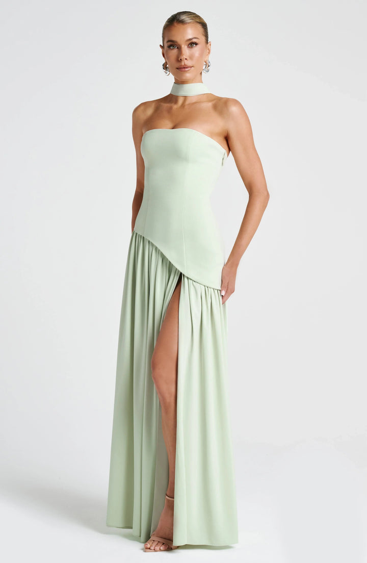 Model wearing a sage green strapless corset maxi dress with a high leg slit and draped scarf detail.