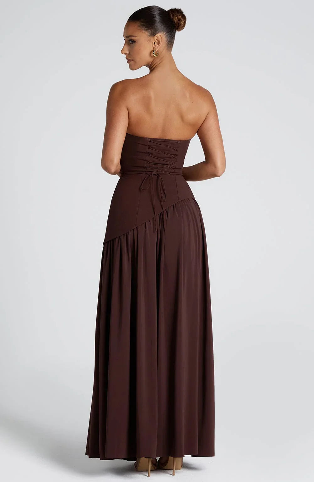 Back view of a chocolate brown strapless corset maxi dress with a lace-up back and flowing skirt.