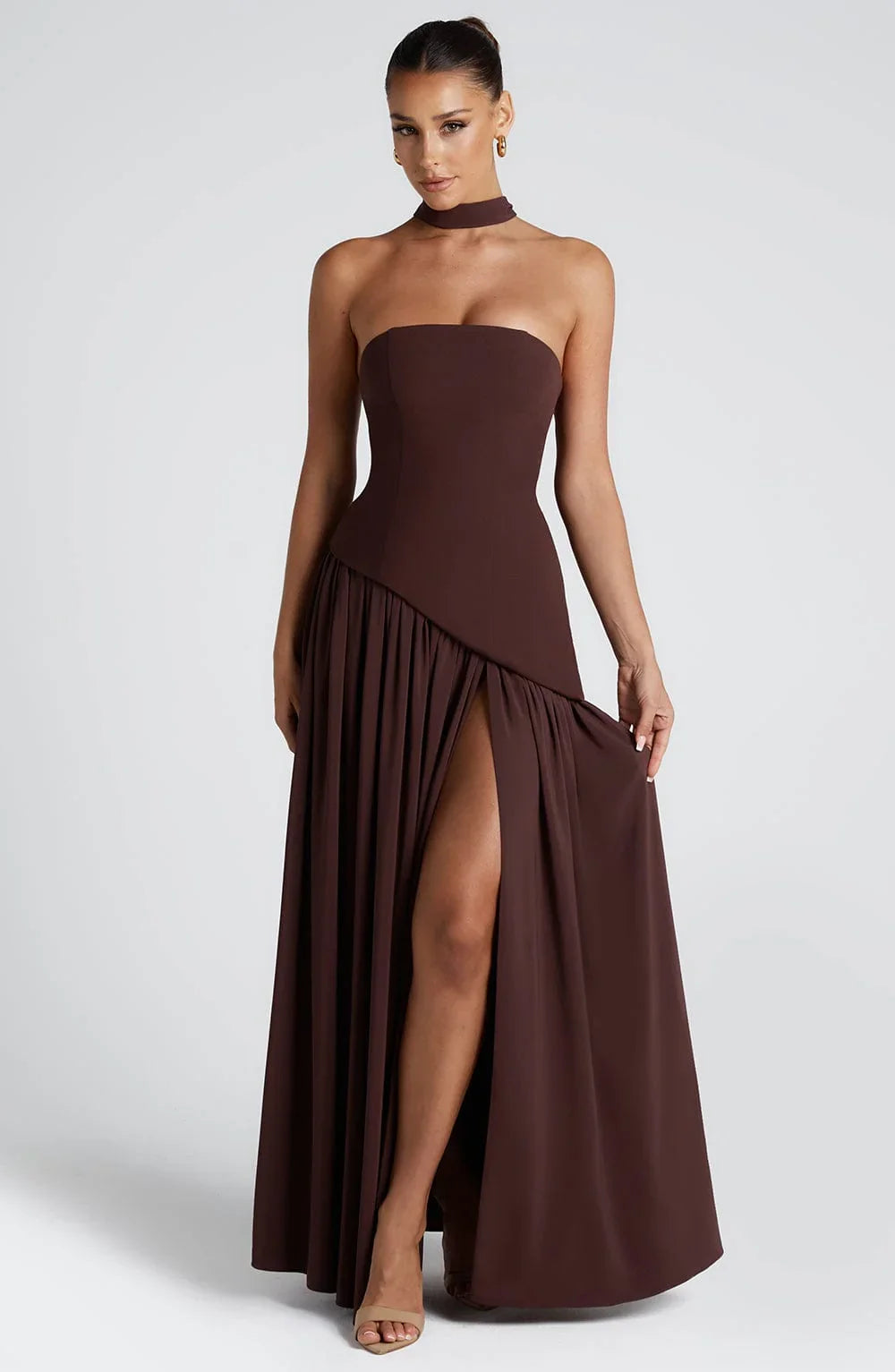 Model wearing a chocolate brown strapless corset maxi dress with a high leg slit and matching scarf detail.
