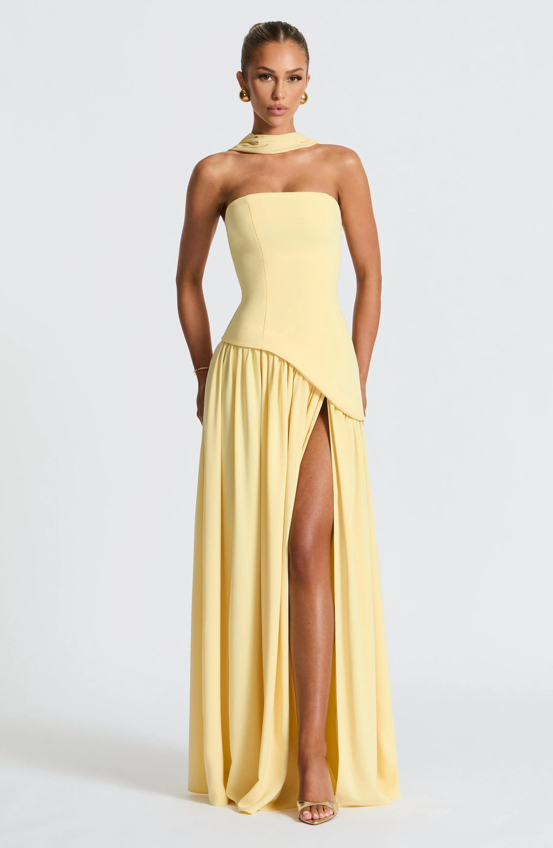 Model wearing a pale yellow strapless corset maxi dress with a high leg slit and draped scarf detail.