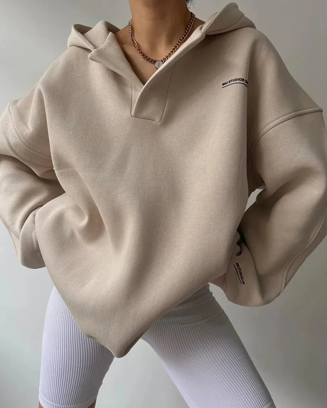 Beige oversized V-neck pullover hoodie with drop shoulders, ribbed cuffs, and subtle chest text branding.