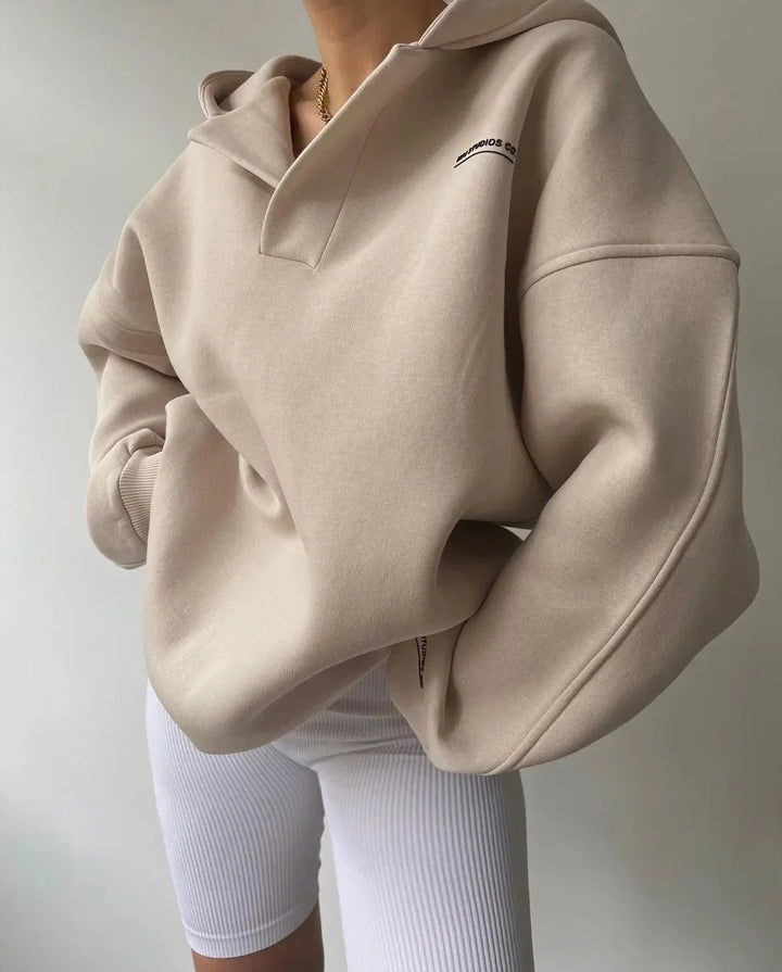 Beige oversized V-neck hoodie with drop shoulders, ribbed cuffs, and subtle chest text, styled with white ribbed leggings.