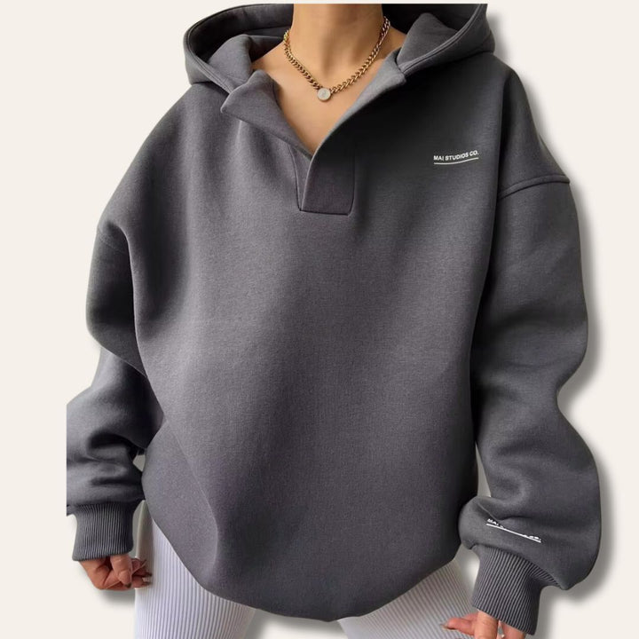Charcoal grey oversized V-neck pullover hoodie with drop shoulders, ribbed cuffs, and subtle white chest branding.