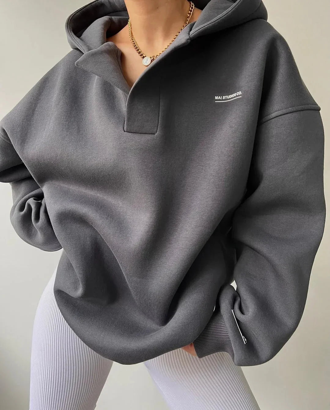 Charcoal grey oversized V-neck pullover hoodie with drop shoulders, ribbed cuffs, and subtle white chest branding.