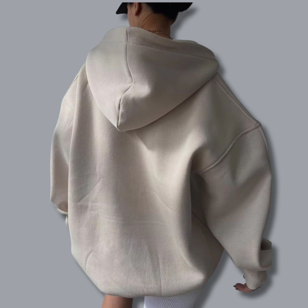Back view of an oversized cream-colored hoodie with a drop-shoulder fit, hood, and ribbed cuffs on a neutral background.