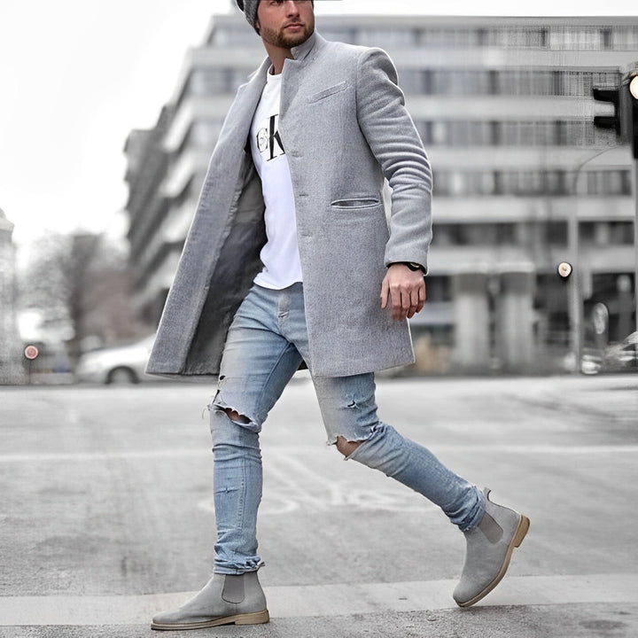 Man wearing a slim-fit grey wool-blend stand collar overcoat with welt pockets, styled with ripped jeans and grey boots.