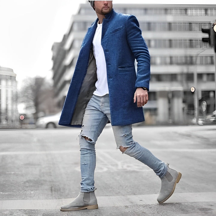 Man wearing a slim-fit blue wool-blend overcoat with a stand collar, white t-shirt, and distressed light-wash jeans.
