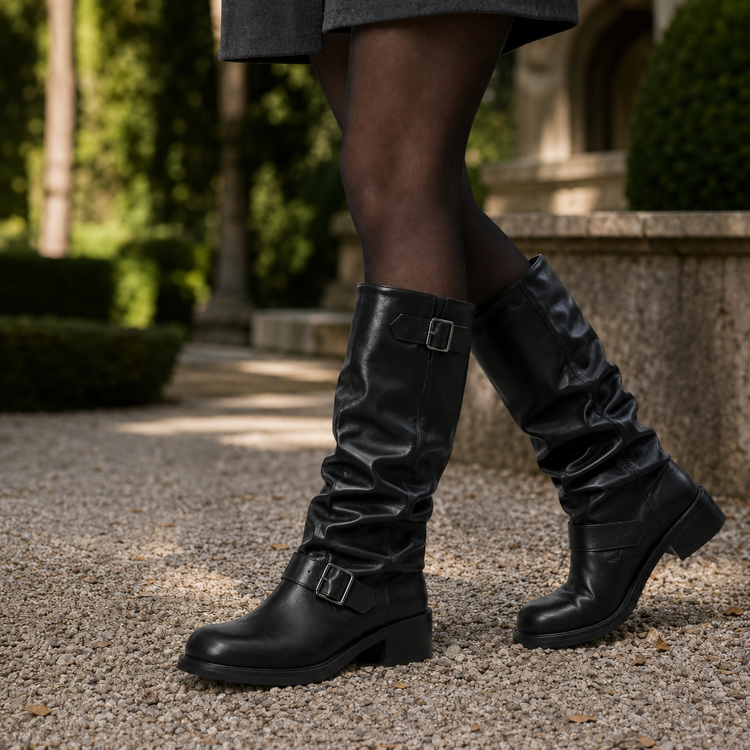 Black faux leather knee-high slouch biker boots featuring double silver buckles and a comfortable low block heel.