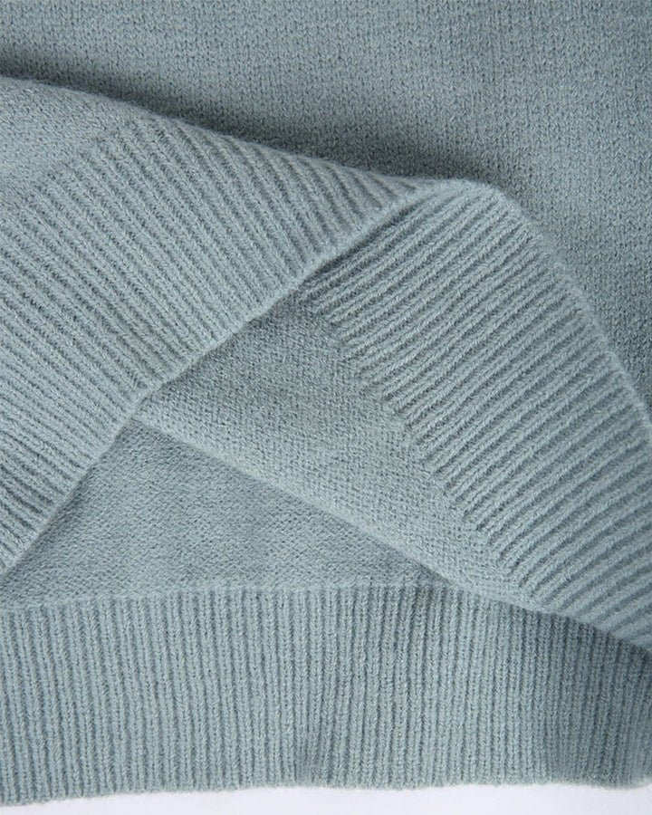 Close-up of a soft, sage green knitted jumper featuring a ribbed hem and textured fabric detail.