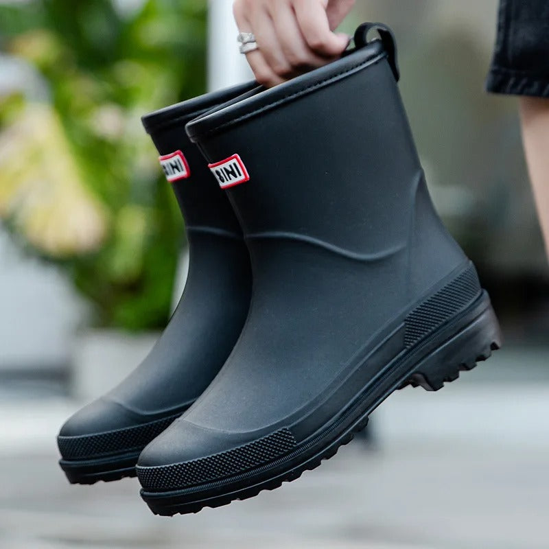 Black waterproof mid-calf rain boots with a grippy treaded sole, back pull tab, and a red brand logo patch.
