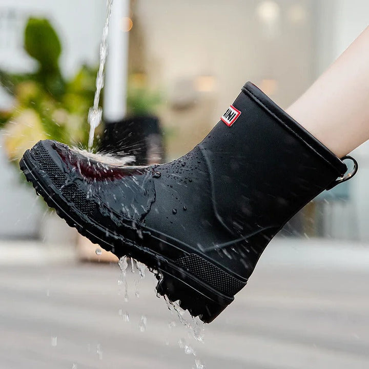 Black waterproof mid-calf rain boot with a grippy treaded sole and back pull tab being tested under running water.