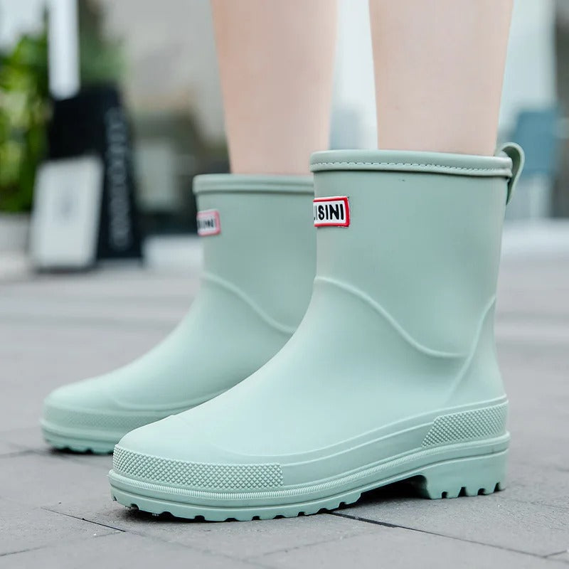 Sage green mid-calf waterproof rain boots with a textured sole, pull tab, and branded patch on the front.