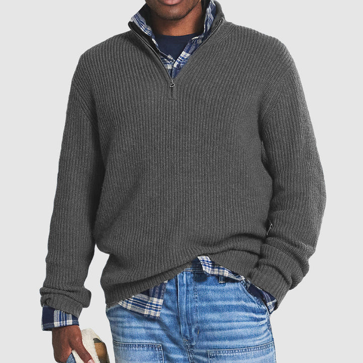 Charcoal grey ribbed knit quarter-zip jumper with a funnel collar, layered over a blue plaid shirt and denim jeans.