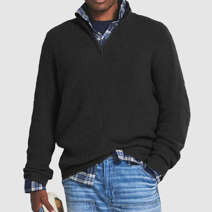 Black ribbed knit quarter-zip jumper with a funnel collar, styled over a plaid shirt and blue jeans.